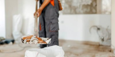 A close up of a young Caucasian man holding a shovel filled with construction residue.